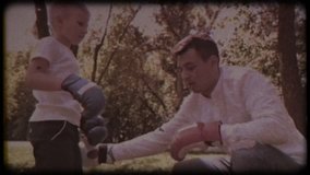 Family video archive. Retro camera 8 mm. Old film. Father and son in boxing gloves play boxing on the lawn near the house. happy childhood.