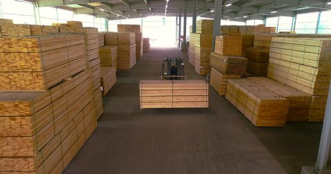A forklift carries a wooden beam through the sawmill's warehouse. Modern warehouse sawmill. A large warehouse of timber materials. Neatly stacked wooden bar in a sawmill warehouse
