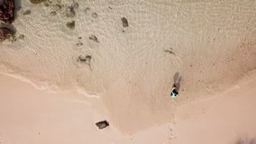 Aerial view of woman in a swimsuit sit leisurely on the beach (Video from drone)