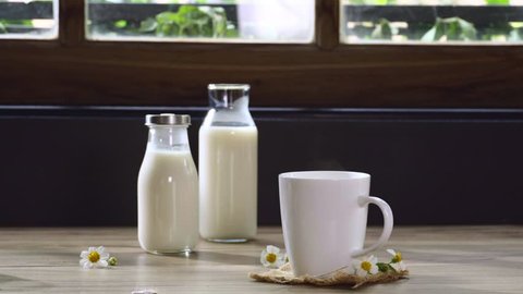 A cup of hot milk with steam and milk bottle on wooden table with view of room on the morning, healthy products by organic natural healthy concept