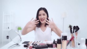 Beauty blogger present beauty cosmetics sitting in front camera for recording video. Happy beautiful young Asian woman use cosmetics review make up tutorial broadcast live video to social network.
