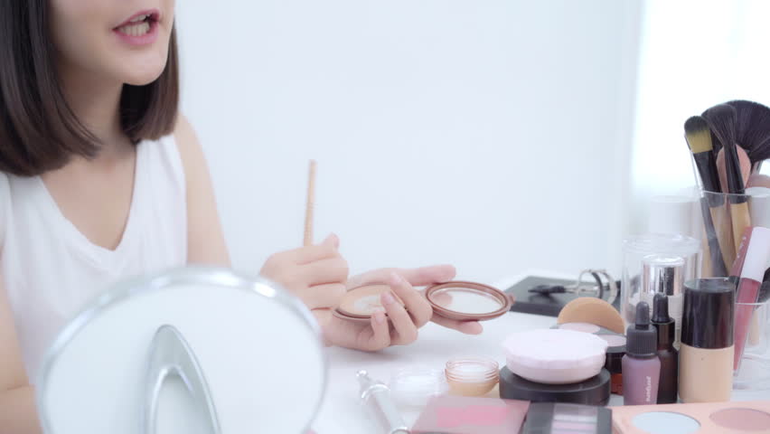 Beauty blogger present beauty cosmetics sitting in front camera for recording video. Happy beautiful young Asian woman use cosmetics review make up tutorial broadcast live video to social network.