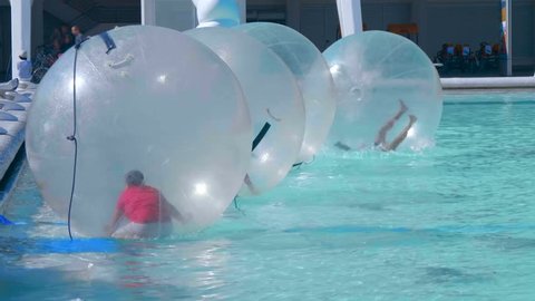 Zorbing, young people have fun inside inflatable balloon balls floating on blue water