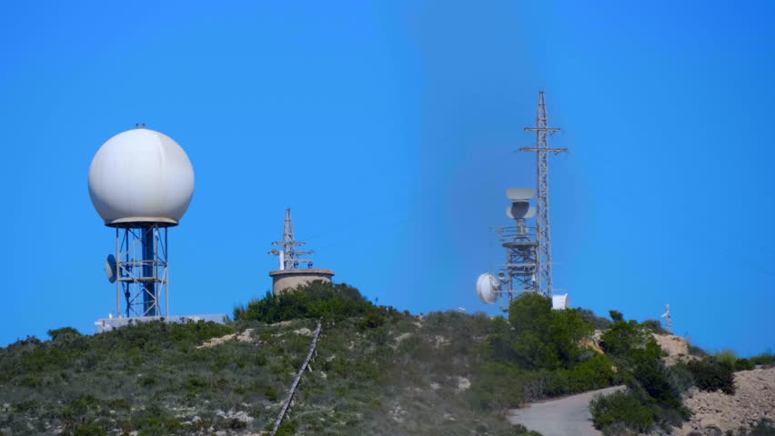 A meteorological radar with a large white sphere on top of a mountain collects weather data from the whole area. Shot in motion
