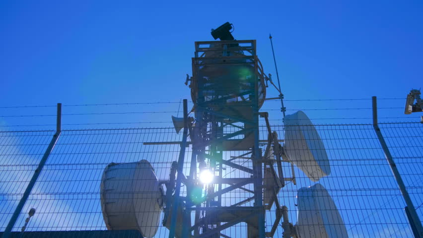 Weather radar with a rotating radiodetection antenna on top of a mountain collects weather data from whole around area against flares in the camera lens. Shot in motion