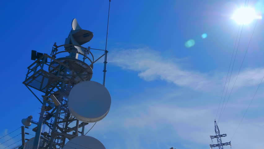 Weather radar with a rotating radiodetection antenna on top of a mountain collects weather data from whole around area against flares in the camera lens | Shutterstock HD Video #1025757872