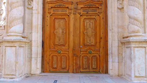 Entrance with a big wooden door in to beautiful ancient church with twisted columns and ornate decorated facade in the Spain city. Shot in motion