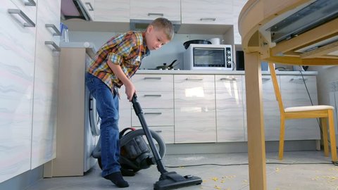 Boy vacuuming the kitchen floor. He tidies up the corn flakes scattered on the gray tile. Side view