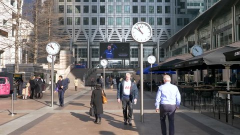 London, England - February 28, 2019: Business Men and women at Canary Wharf durning morning rush hour, with large analog clocks spinning fast, Time and business concept.