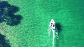 Aerial bird's eye view video taken by drone of speed boat cruising in caribbean tropical beach with emerald - sapphire clear sea