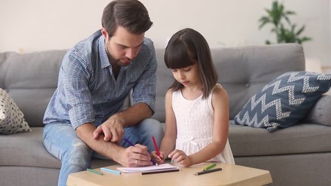 Loving dad and little daughter drawing with pencils at table coloring picture together talking at home, young father teaching helping child girl learning creative activity, parent and kid playing