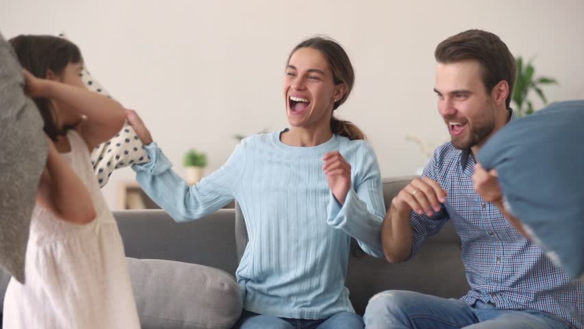 Happy carefree family parents with kid daughter having fun joy pillow fight on sofa enjoying funny leisure activity at home, cheerful mom dad and child girl playing laughing together in living room Royalty-Free Stock Footage #1025766275
