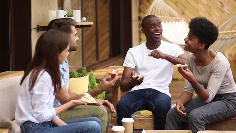 Multicultural happy millennial friends having fun eating sharing pizza together at meeting in pizzeria restaurant, diverse young students joking laughing sitting at cafe table in terrace outdoorの動画素材
