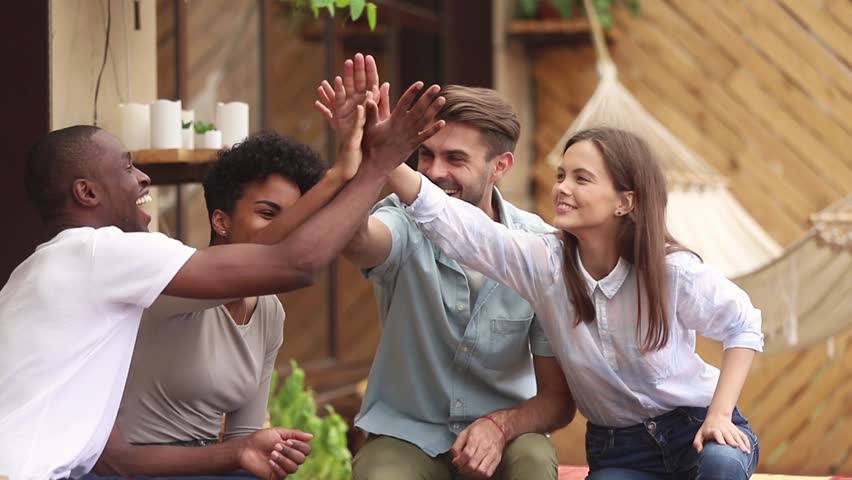 Happy diverse friends students group giving high five celebrating multi-ethnic friendship at meeting outdoor, young multicultural people join hands show unity support having fun making deal together