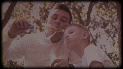 Family video archive. Retro camera 8 mm. Old film. Father with his son blowing soap bubbles, fun family pastime, a child having fun with his dad