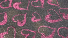 Drawing of many pink hearts with chalk on grey pavement. Real time 4k video footage.