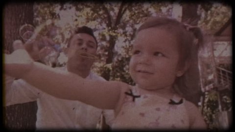 Family video archive. Retro camera 8 mm. Old film. The young father blows soap bubbles with his daughter. Family games near the house. Holiday, holidays. Family together