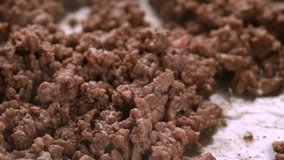 Close slow motion video of browned hamburger meat being stirred in a cooking pan with a wood spoon illuminated with natural lighting.