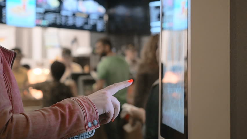 Woman choosing food via self-service machine at fast food restaurant. Girl using touch terminal im Mcdonalds makes a quick order through the self-service. Person swipes the screen making an order | Shutterstock HD Video #1025780381
