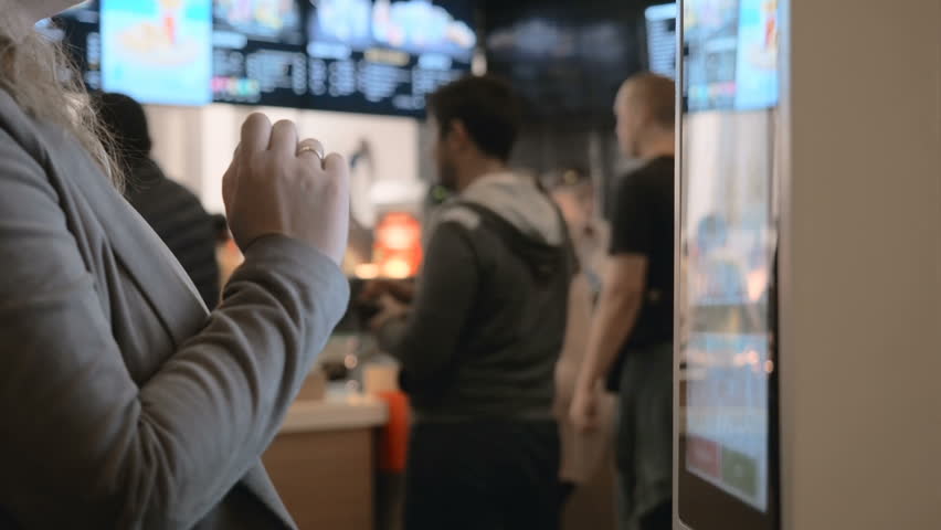 Woman choosing food via self-service machine at fast food restaurant. Girl using touch terminal im Mcdonalds makes a quick order through the self-service. Person swipes the screen making an order | Shutterstock HD Video #1025780384