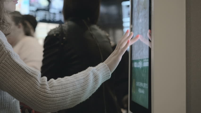 Woman choosing dessert via self-service machine at fast food restaurant. Girl using touch terminal im Mcdonalds makes a quick order through the self-service. Person swipes the screen making an order. Royalty-Free Stock Footage #1025780387