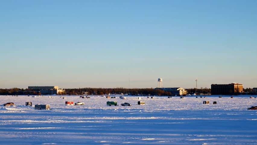 Car drives past Winter Fishing Houses on frozen Lake Bemidji in Minnesota on a late December afternoon in the city of Bemidji, Minnesota.