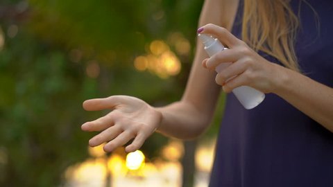 Superslowmotion shot of a beautiful young woman applying an antimosquito repellent spray on her skin. A tropical background. Mosquito defense concept