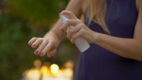 Superslowmotion shot of a beautiful young woman applying an antimosquito repellent spray on her skin. A tropical background. Mosquito defense concept