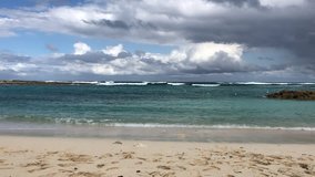 A video of the tropical beach tucked away in the cove with waves in the background and clouds overhead on an island in the Bahamas