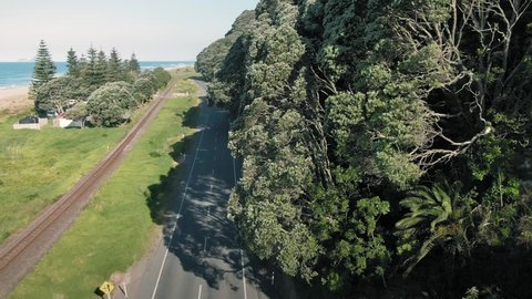 Aerial: Ocean beach and a grove of pohutukawa trees along the coastal road. Pikowau, Bay of Plenty, New Zealand