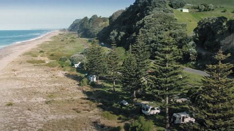 Aerial: Ocean beach and a grove of pohutukawa trees along the coastal road. Pikowau, Bay of Plenty, New Zealand 