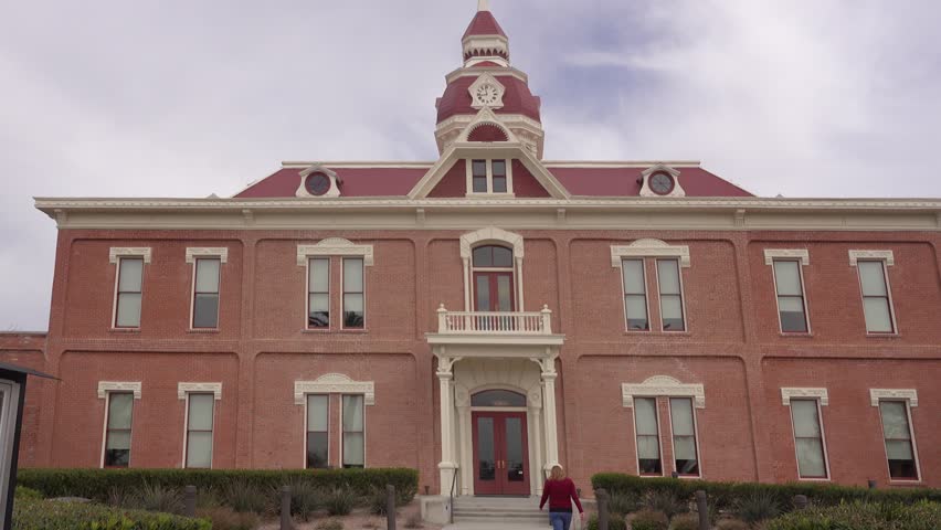A day exterior establishing shot of the historic courthouse in Florence, Arizona. A woman walks into the building.	 	