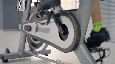 Woman legs spinning pedals on the spin bike. Seamless loop, woman spinning pedals on the static bike, Cycling workout concept. Close-up rotation pedal indoor bike cycling