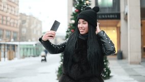 winter, christmas, people concept- Girl making selfie using mobile outdoor at Christmas day decoration light exposure background. Selfie time, blogger is making video and photo for her socialpage.