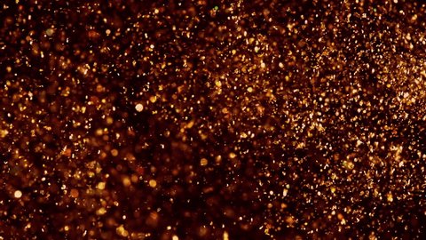 Gold shining sparkles on black. Beautiful abstract texture. Copper particles move chaotically under water. Golden background. Can be used as transitions in projects