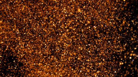 Copper particles move chaotically under water. Golden background. Gold shining sparkles on black. Beautiful abstract texture. Can be used as transitions in projects.