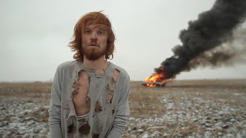 Surviving man on the background of a burning car in the field. Car crash