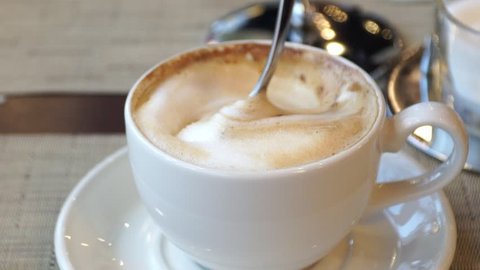 Close-up of cappuccino coffee cup stirred with spoon