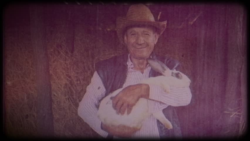 A farmer in a straw hat holds a rabbit in his hands. Farm animals. Raising animals for meat. Portrait of an elderly farmer. Agriculture. Organic food. Ranch. Not vegetarianism, but meat-eating