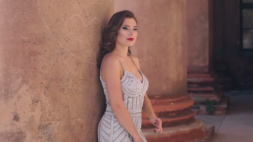 Beautiful sexy elegant lady with hairstyle, make-up and in evening dress stands against the background of the old columns of the old mansion. Portrait of an elegant lady in a dress in the fall.