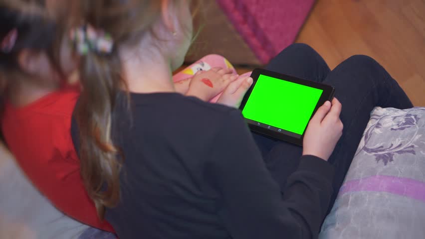 Two girls look at the tablet with a green screen