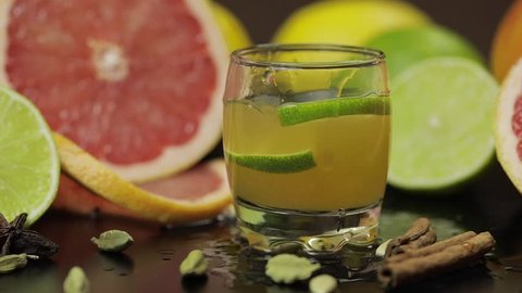 Lime slice falls into a glass cup with an alcoholic cocktail. Fresh fruits in the background. Lime Grapefruit. Prepare a cocktail of whiskey, cognac or liqueur. Slow motion