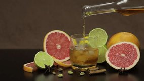 Pour liquor from a bottle into a glass cup with ice cubes. Fresh fruits in the background. Lime Grapefruit. Prepare a cocktail of whiskey, cognac or liqueur. Slow motion - Powered by Shutterstock - Get 15% off with code: PIKWIZARD15