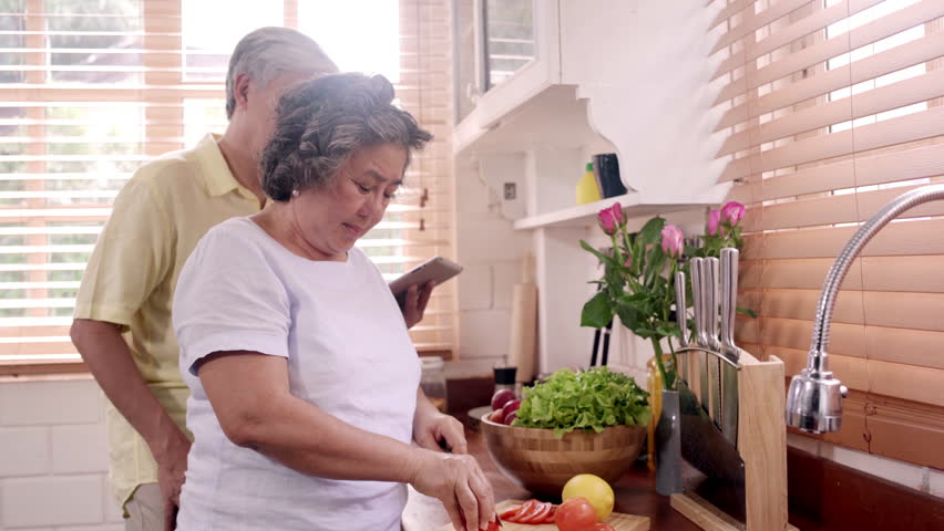 Asian elderly couple cut tomatoes prepare ingredient for making food in the kitchen, Couple use organic vegetable for healthy food at home. Lifestyle senior family making food at home concept. Royalty-Free Stock Footage #1025833907
