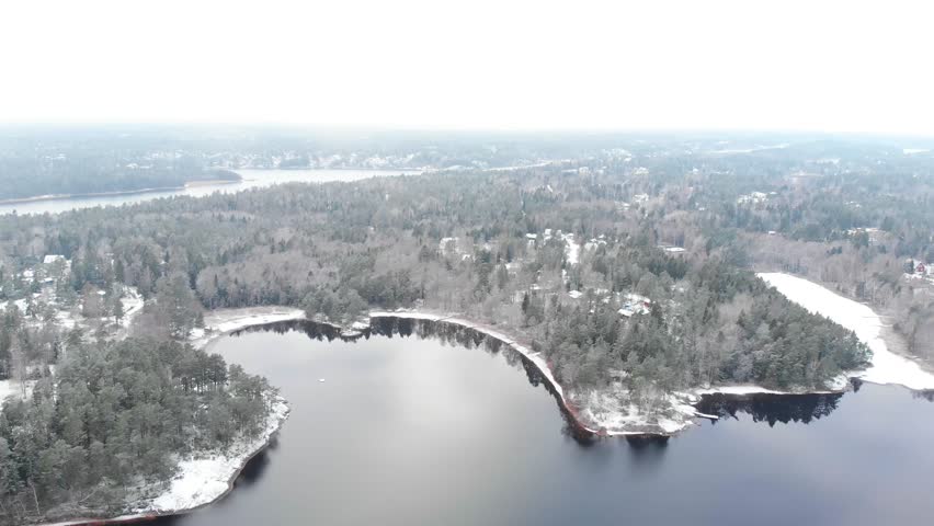 Drone aerial view over frozen shore and houses, trees and a beautiful lake inside clouds