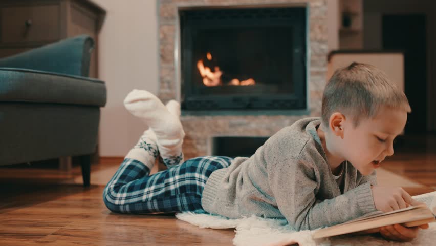 happy child reading a book at home, near the fireplace, Christmas time