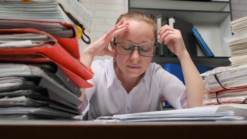 Tired businesswoman working with documents in office, she sits at desk filled with documents. concept of work overtime and deadlines. | Shutterstock HD Video #1025847206