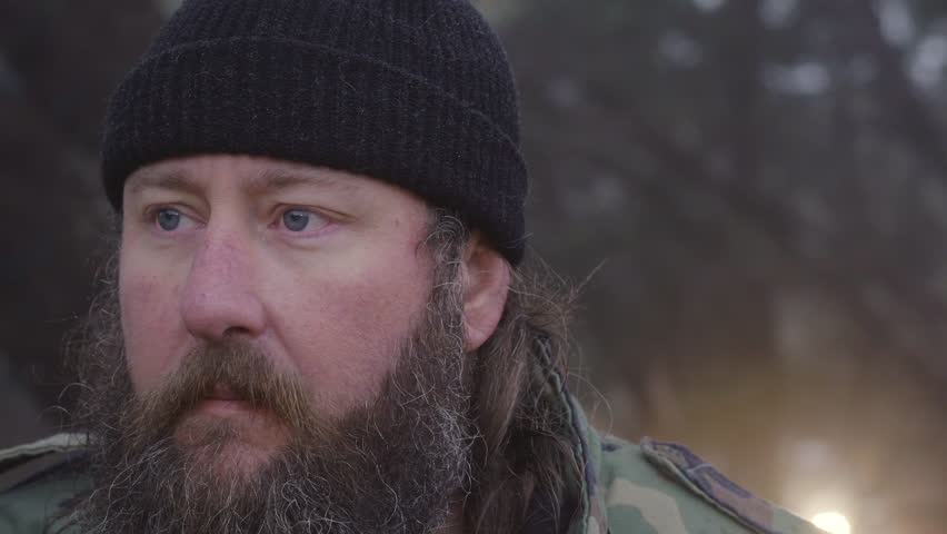 Close up of a male hunter wearing camouflage looking & listening for wildlife in the woods during winter, 60 fps.