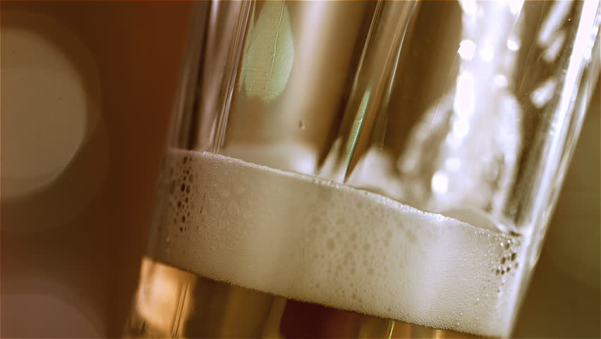 Beer is pouring into angled glass. IPA on tap. Cold Light Beer in a glass with water drops. Craft Beer forming waves close up. Freshness and froth. Bar background. Microbrewery craft beer. | Shutterstock HD Video #1025849783
