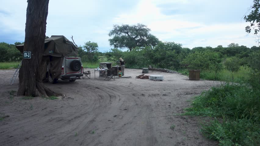 Wide of African Campsite place with a 4x4 Cruiser and Young Woman cleaning